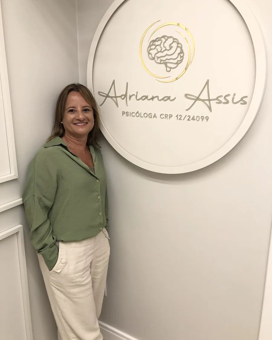 Adriana Assis ao lado do painel com o seu nome e CRP, na recepção do consultório