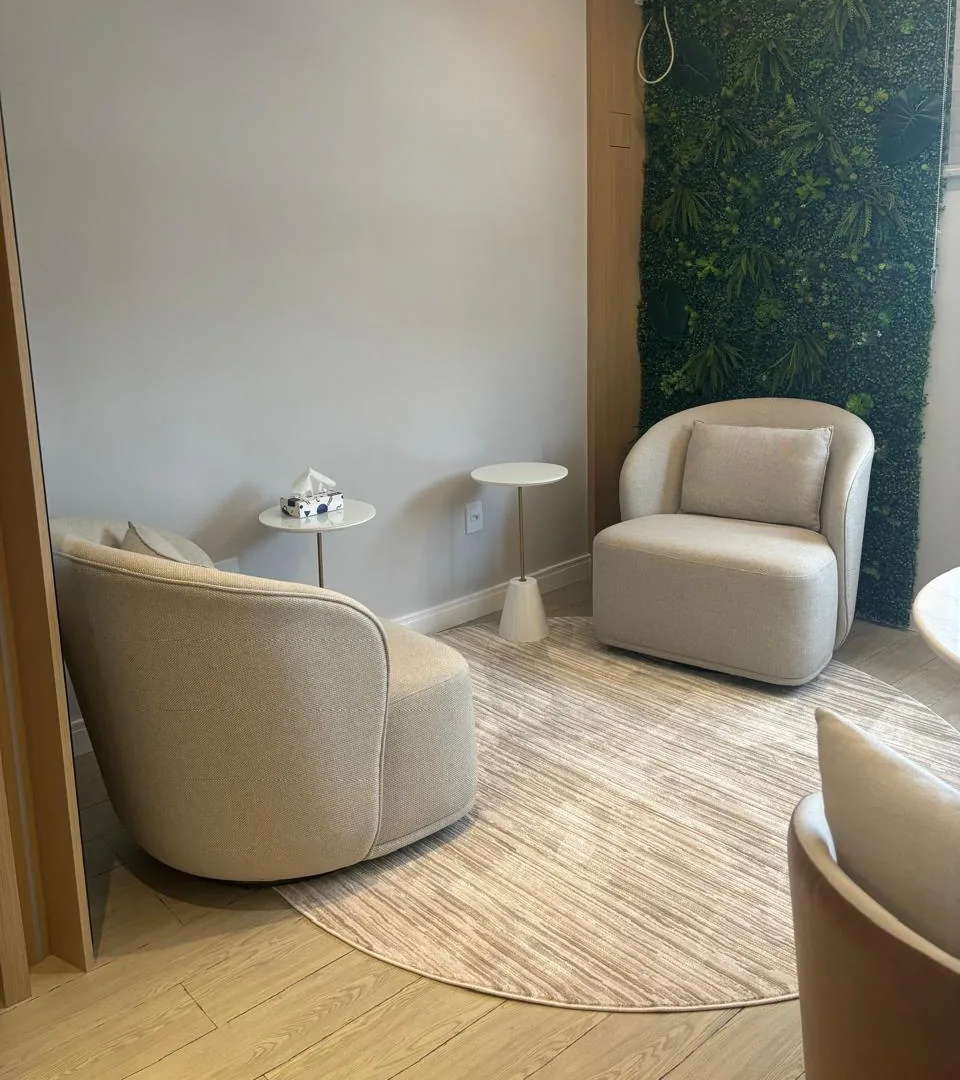 Sala de psicoterapia com duas poltronas claras e uma parede de plantas